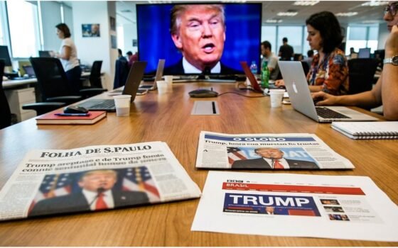 Três jornais abertos com manchetes sobre Donald Trump em uma mesa de redação